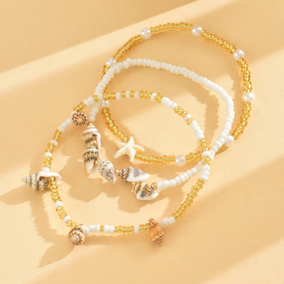 Ensemble de bracelets de cheville dorés avec perles blanches, étoiles de mer et pendentifs coquillage.