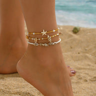 Ensemble de bracelets de cheville dorés avec étoile et coquillages perlés portée sur la plage.