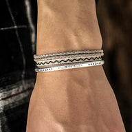 Trio de bracelets tibétains pour homme avec cordes beige et gris et bracelets argentés gravés.