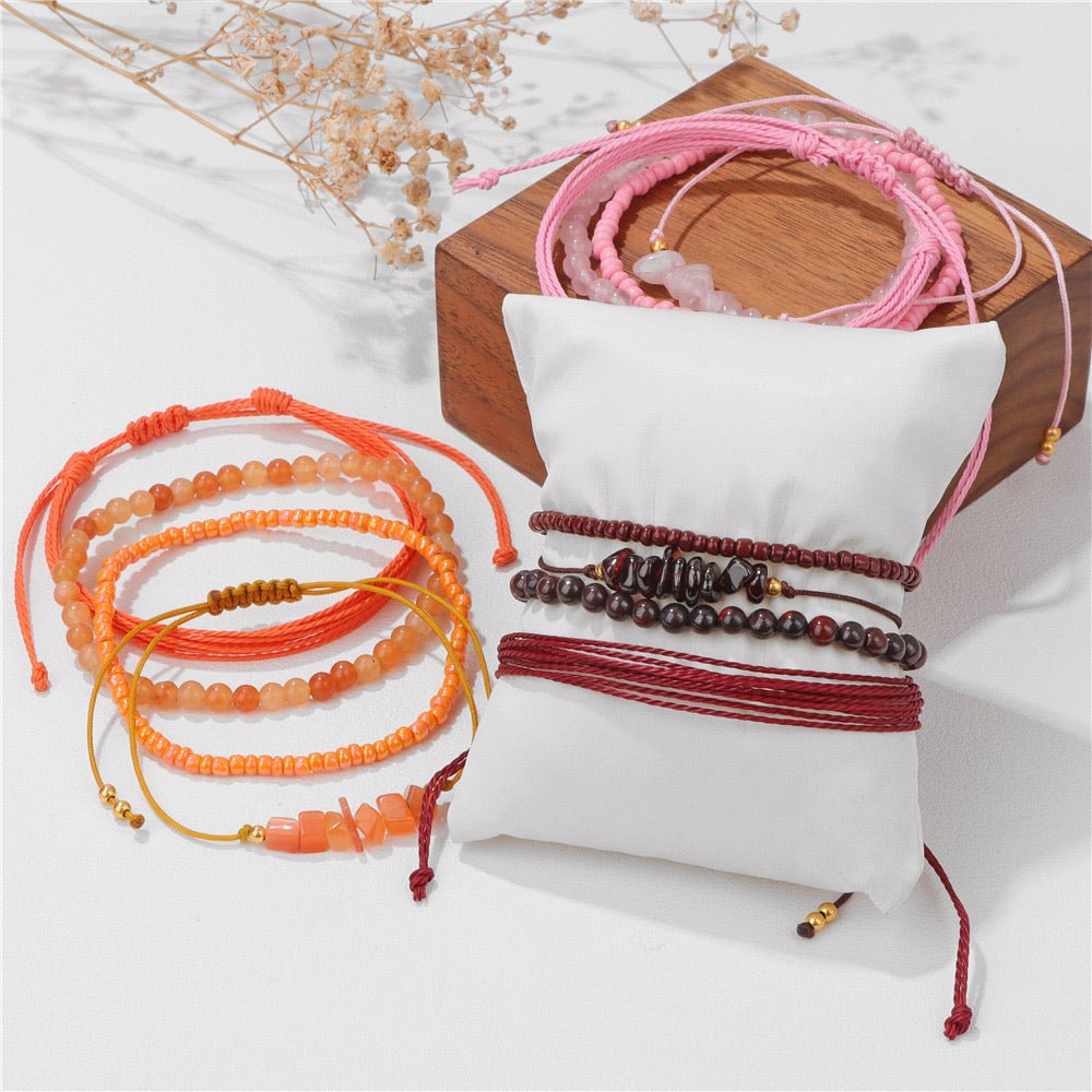 Ensemble de bracelets en pierres naturelles orange et rouge avec perles, sur coussin blanc et boîte en bois.