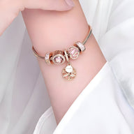 Bracelet argenté avec cinq charms roses et pendentif arbre de vie doré sur poignet féminin.