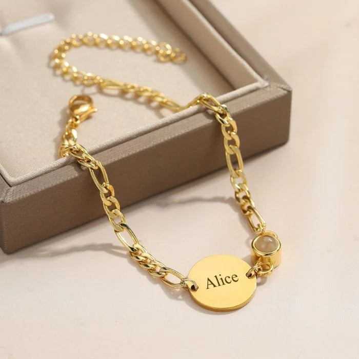 Bracelet doré à mailles figaro avec médaille ovale gravée du prénom Alice et un petit pendentif rond transparent.