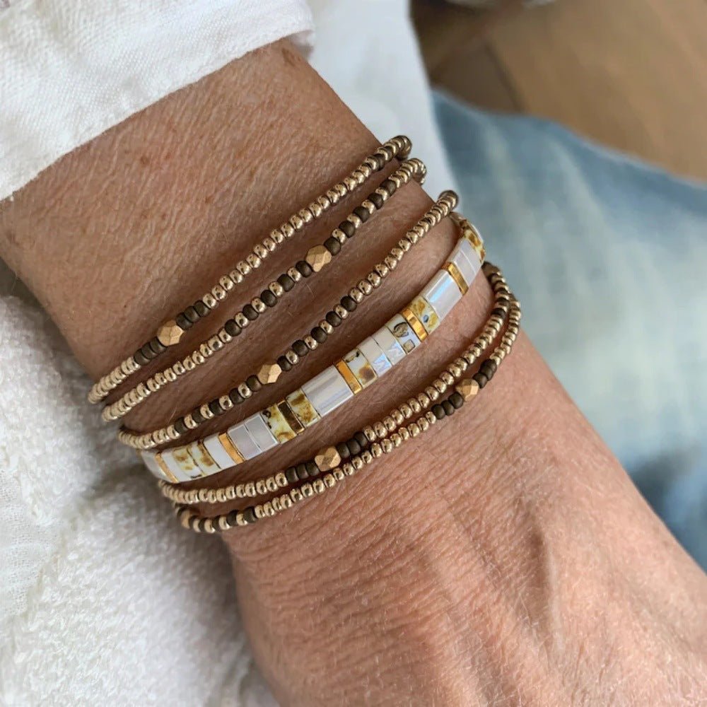 Set de bracelets fins dorés et marron avec perles dorées et cubes marbrés blancs en style bohème chic.