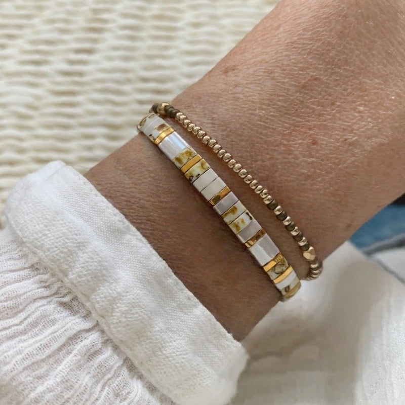 Set de bracelets dorés et blancs avec perles fines et cubes marbrés blancs, style bohème chic.