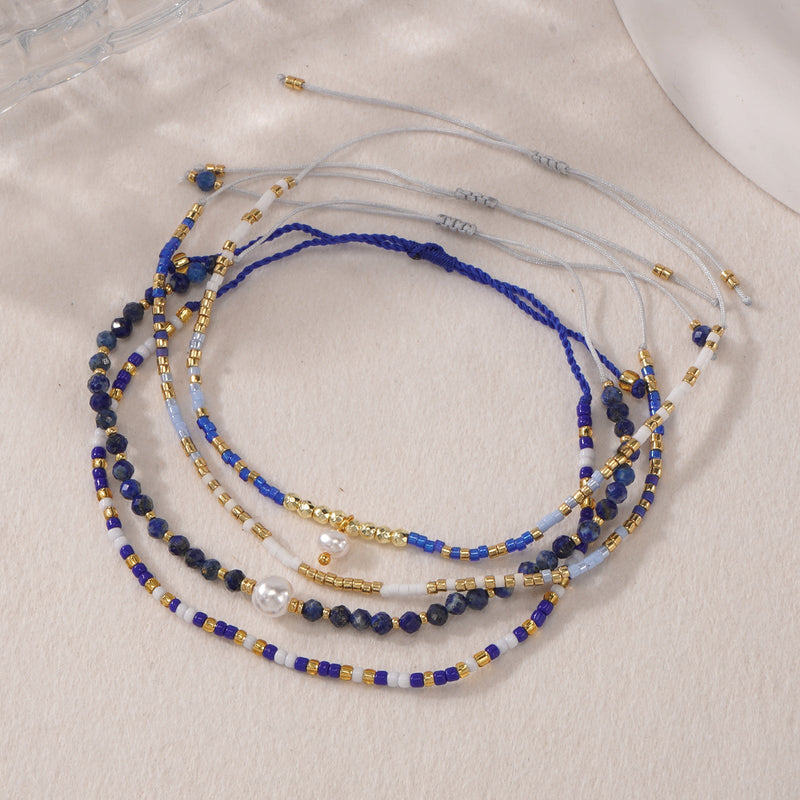 Set de bracelets à perles bleu lapis lazuli et or avec perle blanche, cordon gris coulissant, style bohème chic.