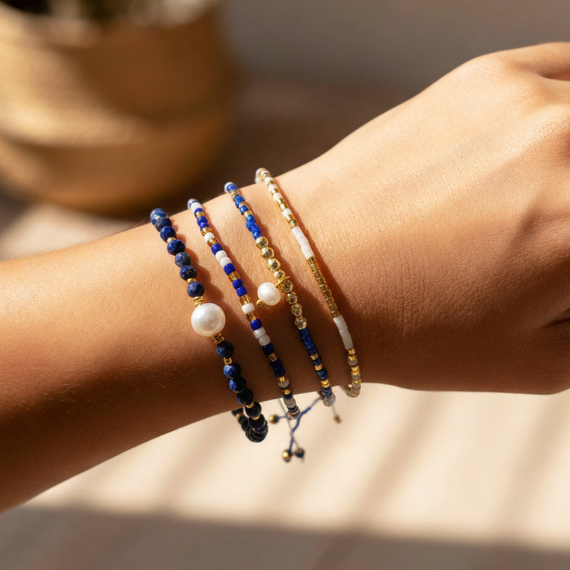 Set de quatre bracelets à perles bleues lapis lazuli, perles blanches et dorées, cordons coulissants fins, style bohème chic.