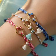 Trio de bracelets cordon bleu, blanc et rouge avec pompons et anneaux dorés élégants.