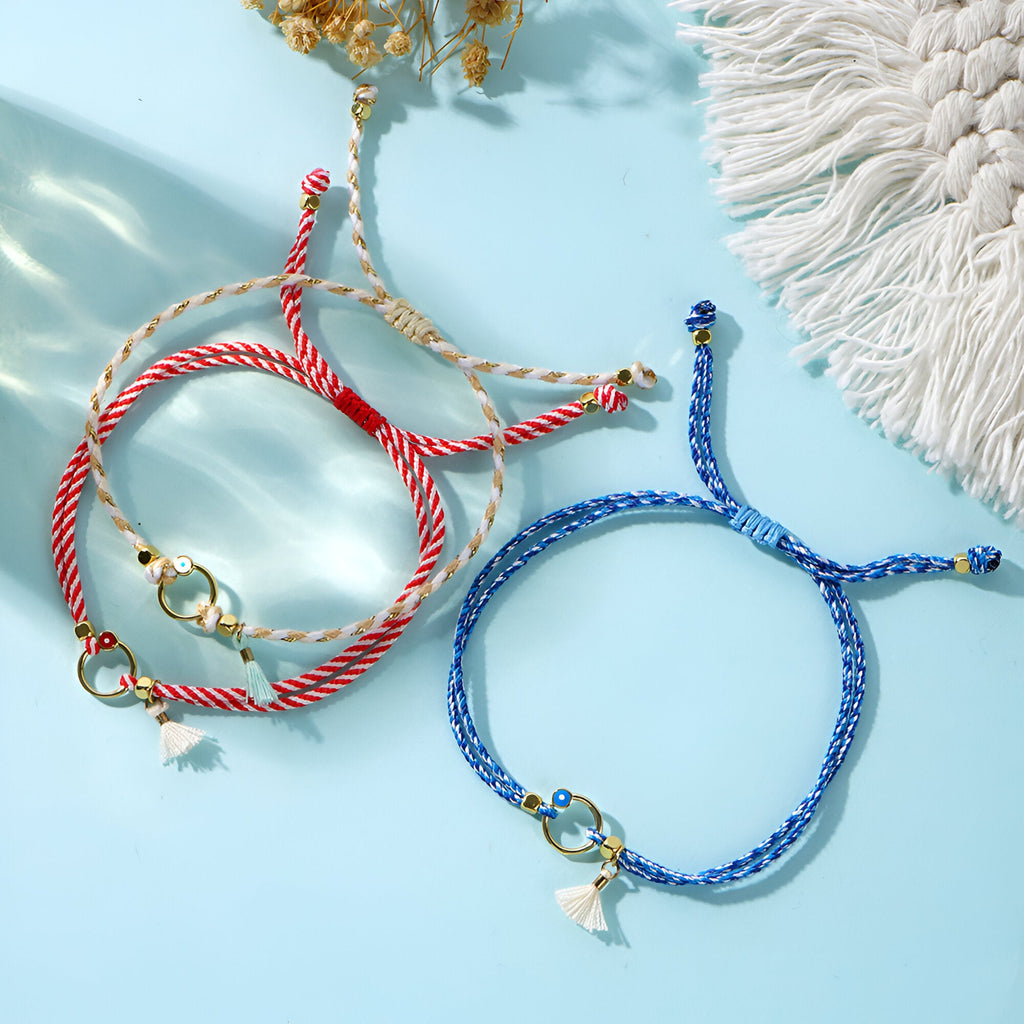 Trio de bracelets cordon bleu, blanc et rouge avec pompons et breloques dorées.