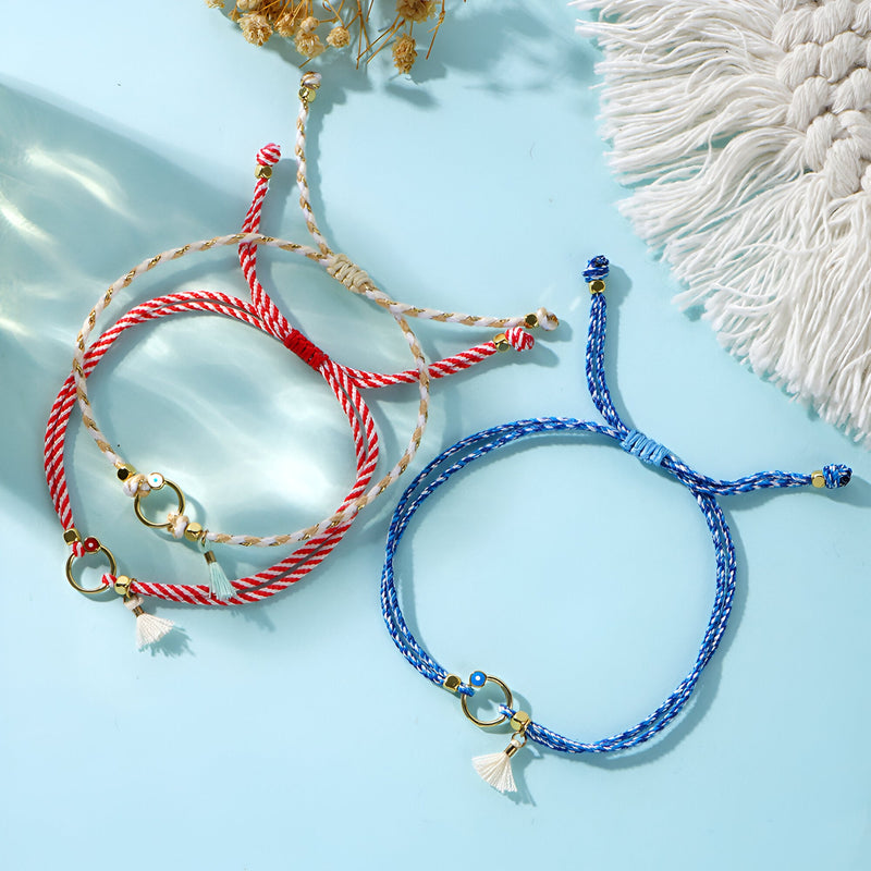 Trio de bracelets cordon bleu, blanc et rouge avec pompons et breloques dorées.