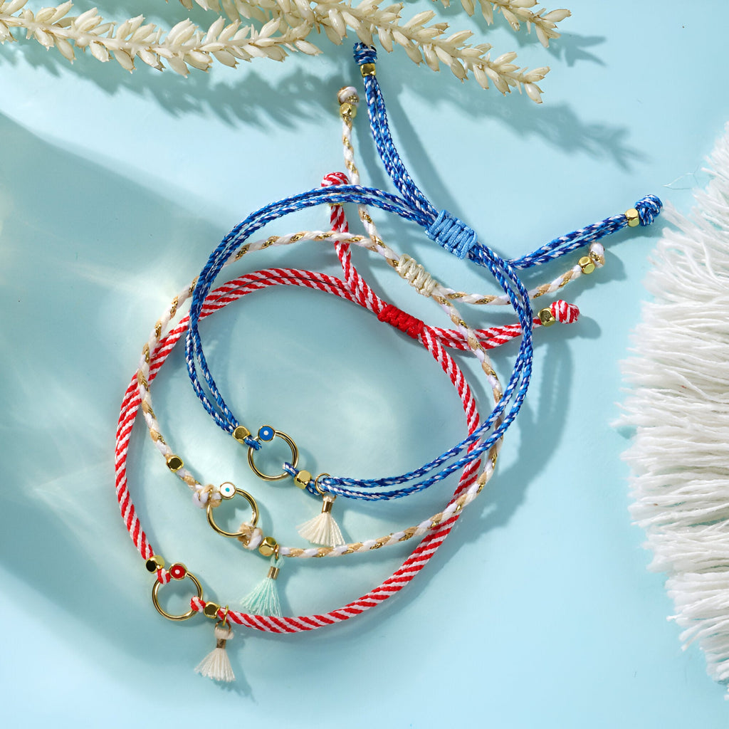 Trio de bracelets cordon bleu, blanc et rouge avec pompons et breloques dorées.