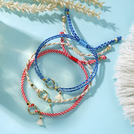 Trio de bracelets cordon bleu, blanc et rouge avec pompons et breloques dorées.