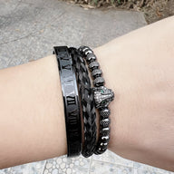 Trio de bracelets noirs en acier avec tête de léopard orné d'yeux verts sur poignet clair.