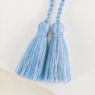 Paire de pompons en fil bleu clair avec tissage détaillé et boucle tressée.