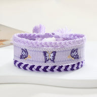 Trio de bracelets en coton tissé violet avec papillons brodés et bordures torsadées foncées.