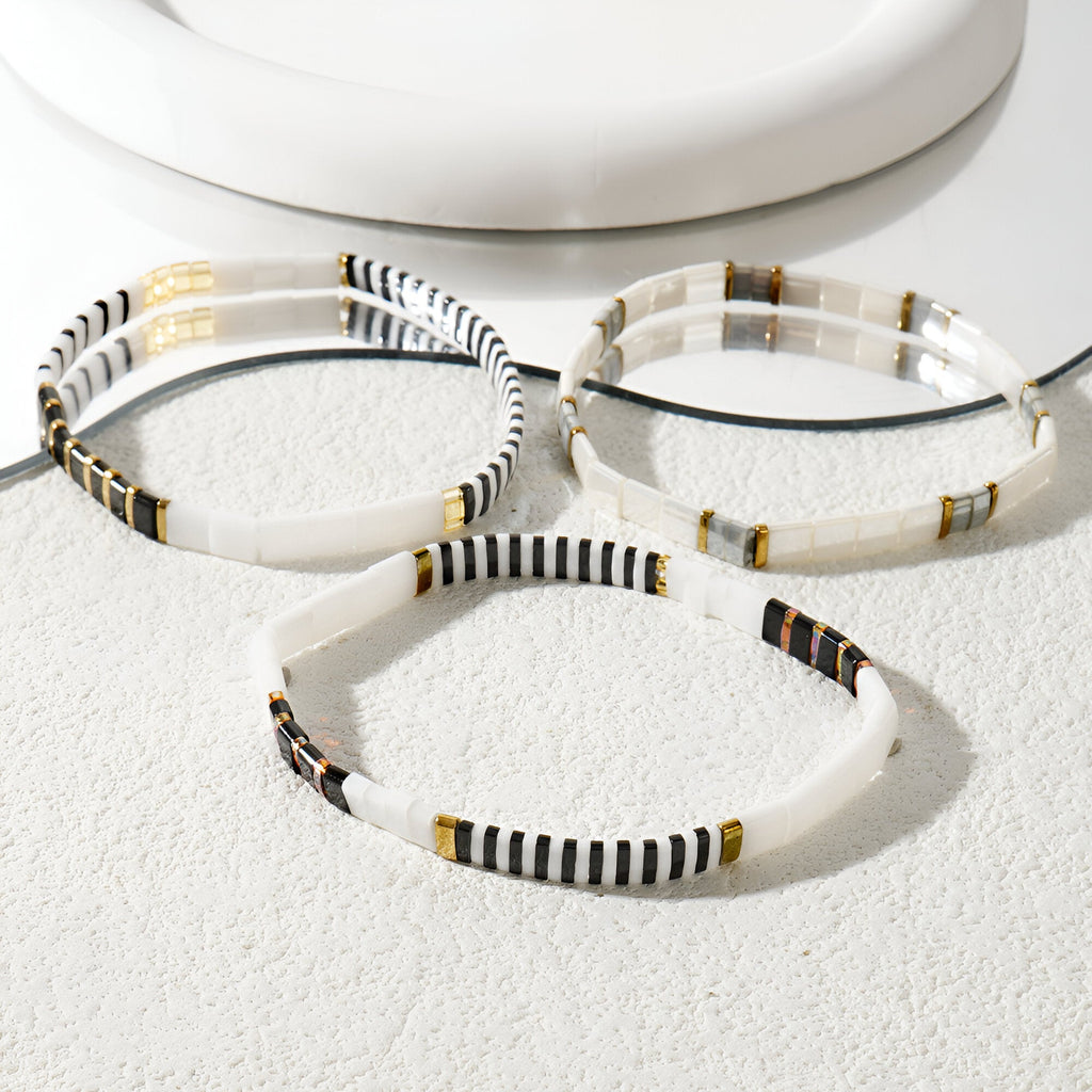Trio de bracelets blancs en perles, motifs noirs et dorés, style délicat et épuré.