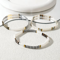 Trio de bracelets blancs en perles, motifs noirs et dorés, style délicat et épuré.