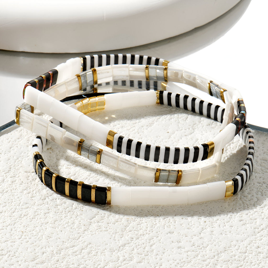 Trio de bracelets en perles blanches, noires et dorées, design rayé élégant et minimaliste.
