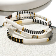 Trio de bracelets en perles blanches, noires et dorées, design rayé élégant et minimaliste.