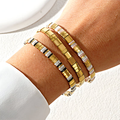 Trio de bracelets en perles dorées et carrées style Japonais, porté au poignet féminin.