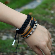 Trio de bracelets larges noirs en cuir, tresse textile et perles cristallines sur poignet féminin.