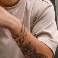 Trio de bracelets maille en titane argentés portés sur poignet masculin avec tatouage noir detailed.