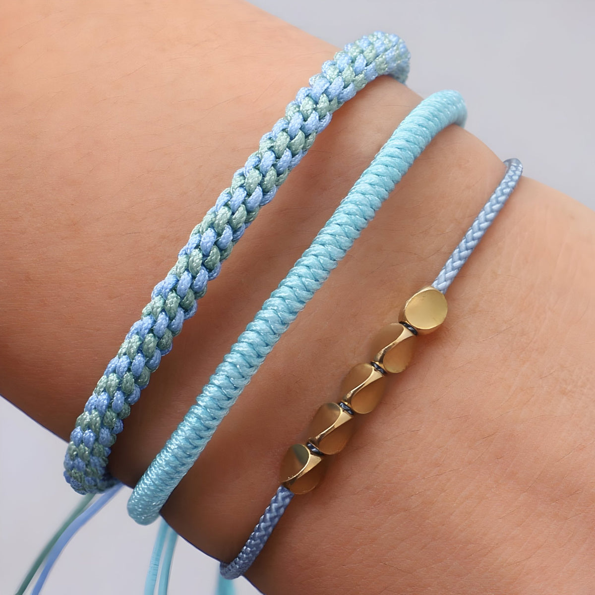Trio de bracelets tibétains bleus en corde tressée avec perles en cuivre doré.