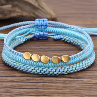 Trio de bracelets tibétains bleus en corde tressée avec perles en cuivre doré, style porte-bonheur féminin.