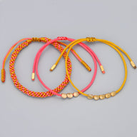 Trio de bracelets tibétains en corde rose, rouge et jaune avec perles en cuivre doré.