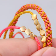 Trio de bracelets en corde rose, jaune et cuivre, détails cercles dorés, design tressé et lisse.