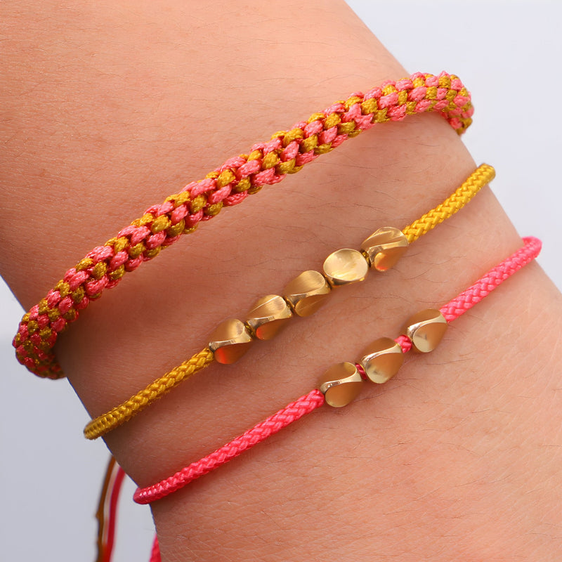 Trio de bracelets tibétains en corde rose, jaune et cuivre, détails en perles dorées.