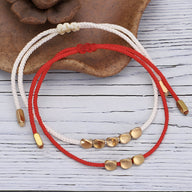 Trio de bracelets tibétains en corde rouge et blanche avec perles de cuivre doré, style minimaliste.