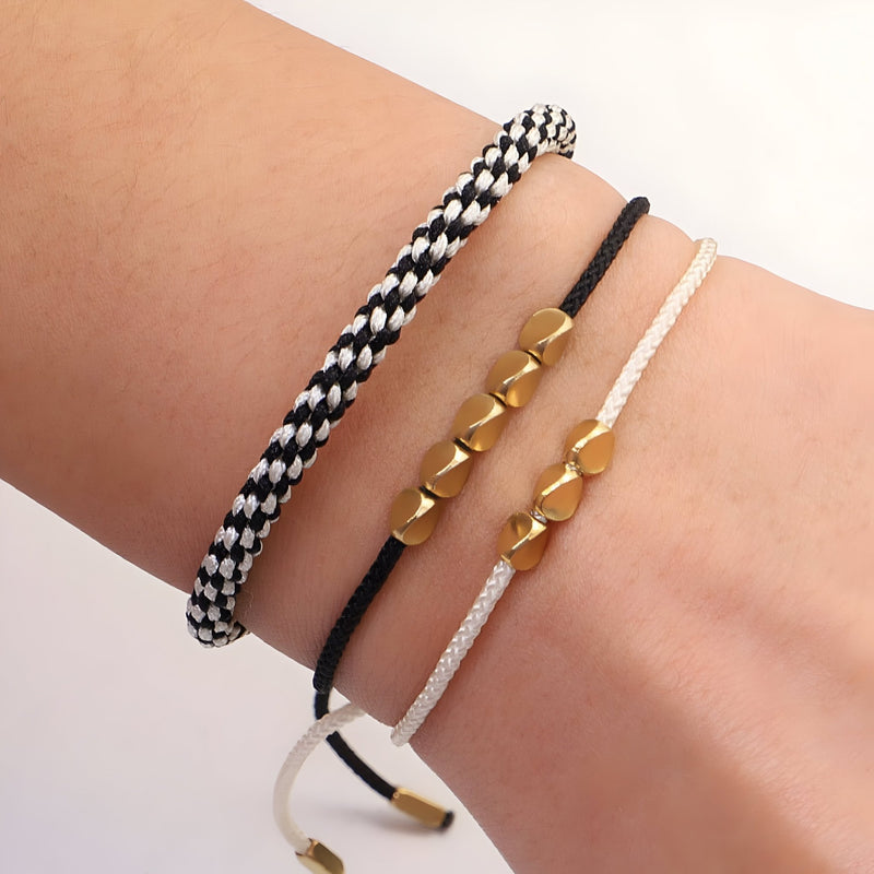 Trio de bracelets tibétains en corde noire, blanche et noir/blanc avec perles cuivrées sur poignet féminin.