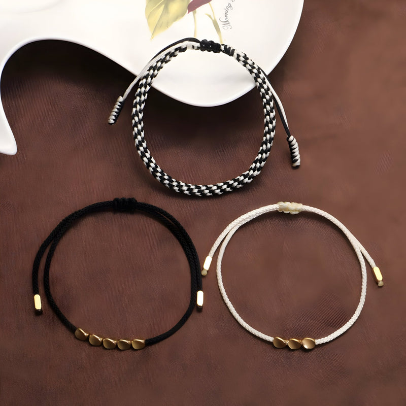 Trois bracelets tibétains en corde avec détails en cuivre, couleurs noir et blanc, noir, et rose pâle, style minimaliste.