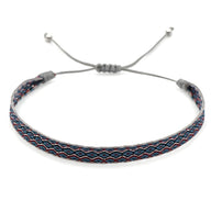 Bracelet tibétain tissu bleu avec motifs rouges et blancs, ajustable avec cordon gris et perles en argent.