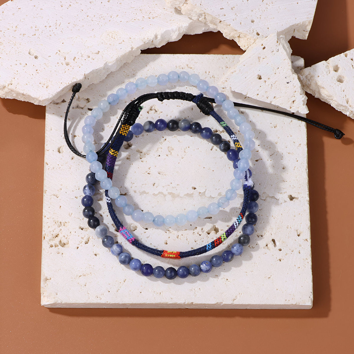 Trio de bracelets tibétains bleu calcédoine avec perles, cordon ajustable et détail en métal rouge et doré.