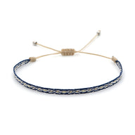 Bracelet tibétain bleu en coton tressé avec motifs argentés et fermeture ajustable beige.