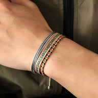 Trio de bracelets tibétains multicolores en coton tressé et argent avec motifs gravés, porté au poignet.