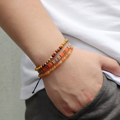 Trio de bracelets tibétains en jaspe rouge et orange avec perles et cordon réglable porté au poignet.