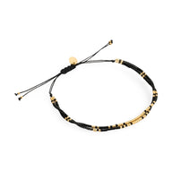 Bracelet fin ajustable en perles noires et dorées avec détails métalliques élégants.