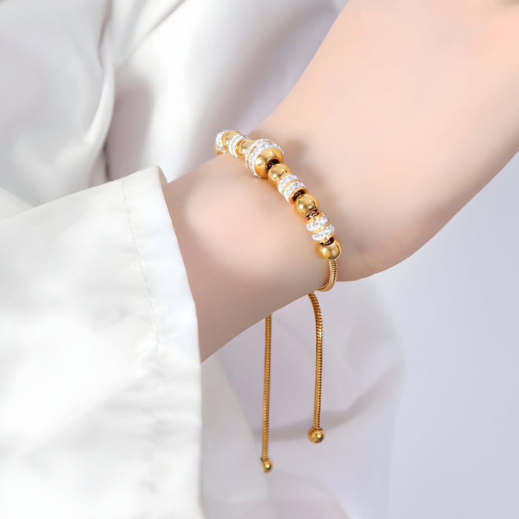 Bracelet ajustable en titane plaqué or avec perles et cristaux scintillants portée au poignet.