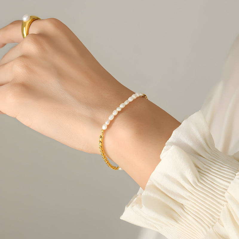 Bracelet fin doré avec une rangée de perles d'eau douce sur un poignet féminin, style élégant.