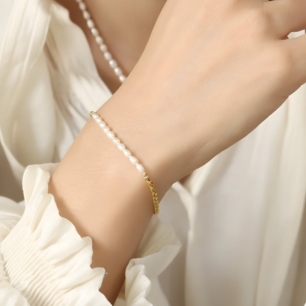 Bracelet fin en maille dorée avec perles d'eau douce blanches porté sur poignet féminin.