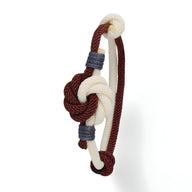 Bracelet cordon bicolore rouge et blanc avec noeud central et détails gris en corde tressée.