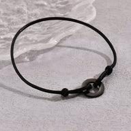 Bracelet cordon noir pour homme avec charm arrondi en métal sombre.
