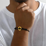 Bracelet cordon noir pour homme avec charm arrondi en métal doré, style minimaliste.