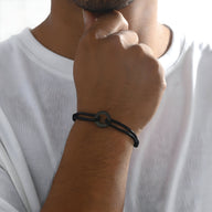 Bracelet homme cordon noir avec charm arrondi en métal noir mat sur poignet.