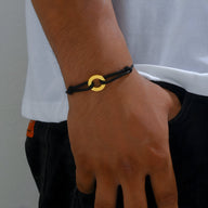 Bracelet cordon noir homme avec charm arrondi en métal doré, style minimaliste.