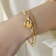 Bracelet double en titane plaqué or avec motif cœur et chaîne fine élégante, porté au poignet.