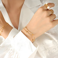 Bracelet double en titane plaqué or à petits cubes, porté avec bagues assorties sur main féminine.