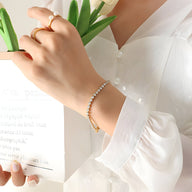 Bracelet fin en titane or avec petites pierres de zircon scintillantes porté au poignet.